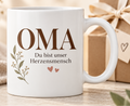 Weiße Tasse mit Aufschrift OMA – Du bist unser Herzensmensch und Blumenranke
